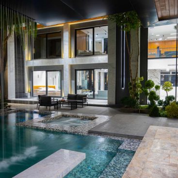 A contemporary home featuring a sleek pool and an inviting patio area, surrounded by lush greenery.